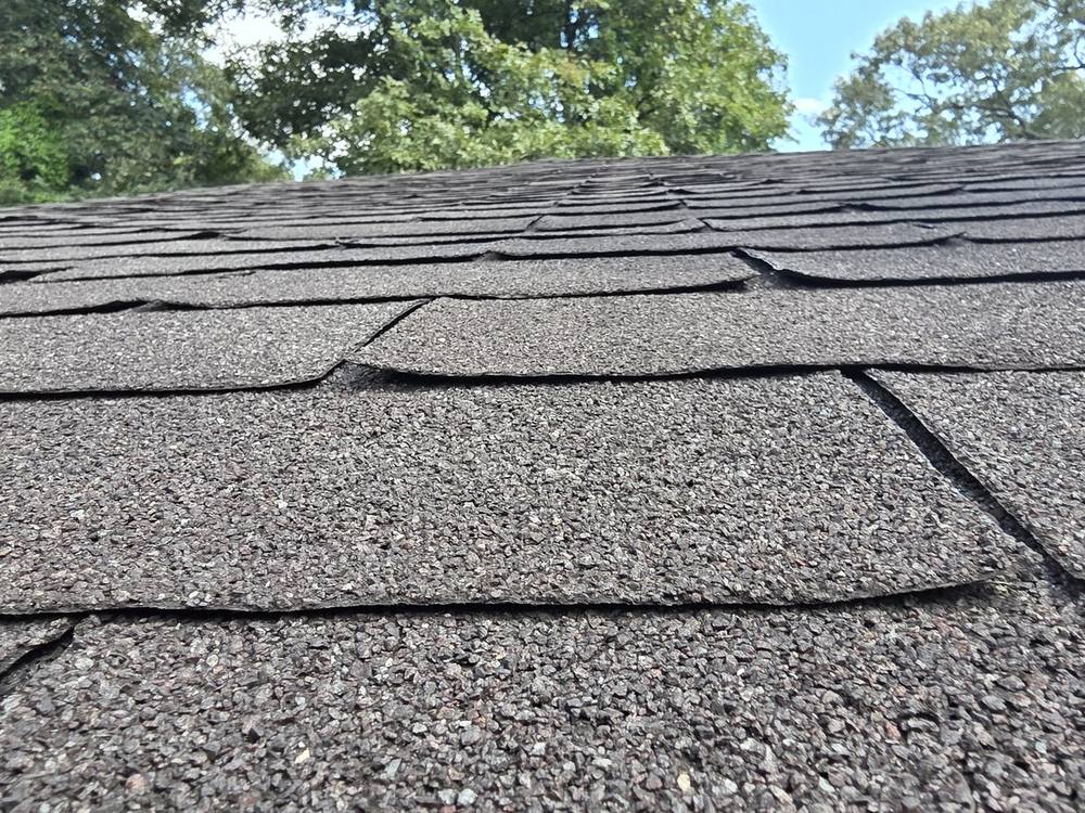 Asphalt shingles at a roof eave with cracked courses that no longer lie flat